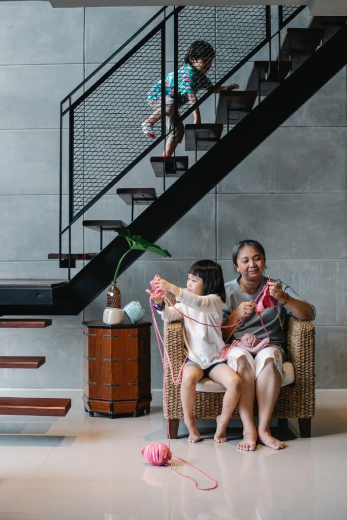Woman and girl knitting on a chair while another child climbs stairs in a modern home.