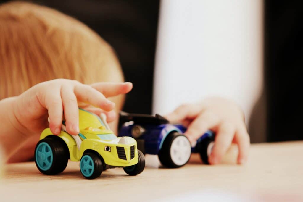 A child playing with yellow and blue toy cars on a light-colored surface.