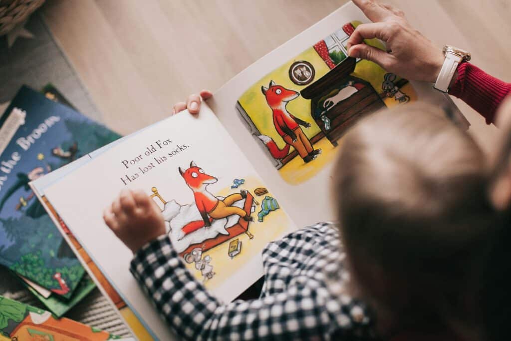 Child reading a picture book about a fox with an adult, showing bright illustrations of the fox's story.