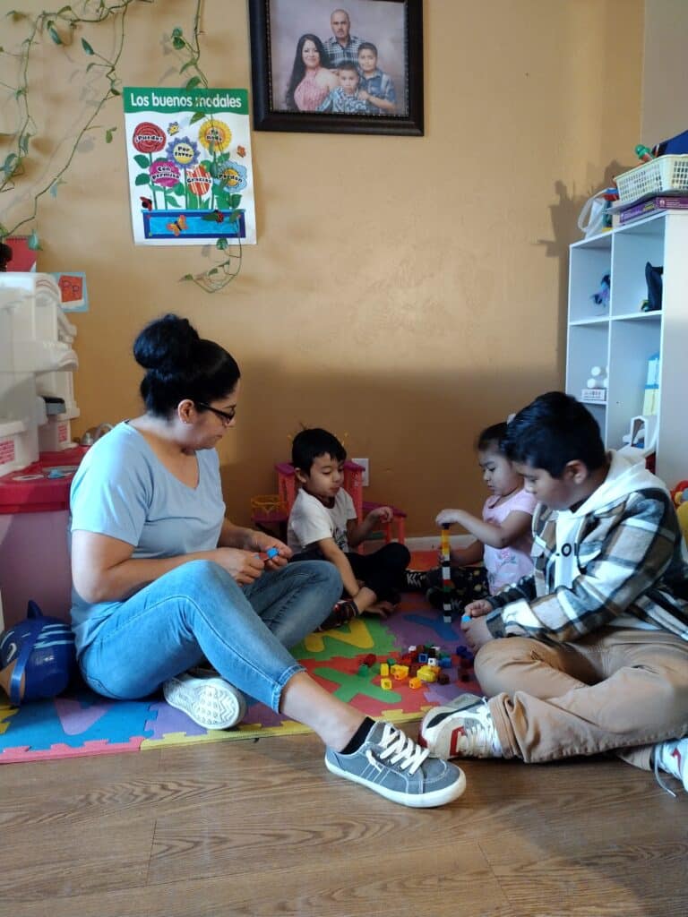 A woman and three children play with building blocks on a colorful mat in a cozy room.