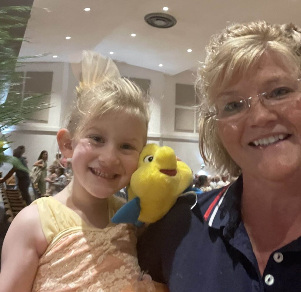 Smiling woman and young girl holding a yellow plush toy, posing together in a bright indoor setting.