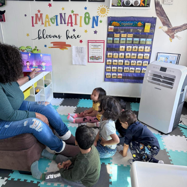 A teacher reads to a group of young children sitting on the floor in a colorful classroom.
