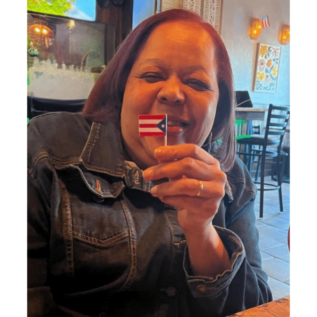 Woman smiling and holding a small Puerto Rican flag while sitting in a restaurant.