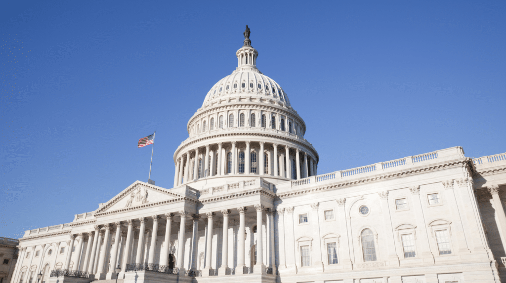 The United States Capitol building with an American flag against a clear blue sky.