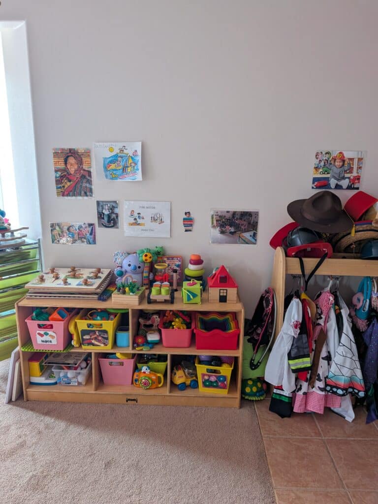 A wooden toy shelf with bins of toys, topped with various children’s drawings and photos on the wall.