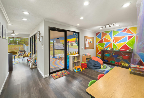Colorful children's playroom with geometric mural, toys, bookshelves, and a table with small chairs.