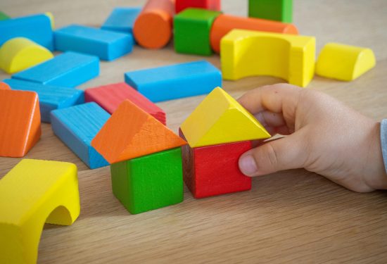 A child’s hand playing with colorful wooden building blocks on a wooden surface.