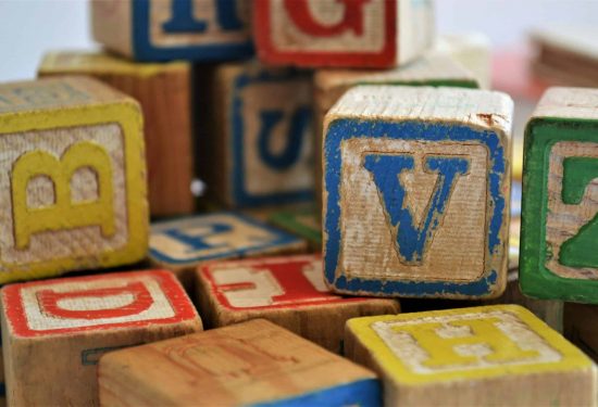 Close-up of colorful wooden alphabet blocks, some showing letters like V, B, Z, H, and D.
